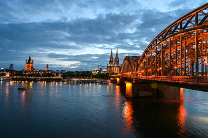 Keln, Njemačka. Čuveni Hohenzollernov most. Zgrade u historijskom centru grada. Tornjevi katedrale i gradske vijećnice noću.
