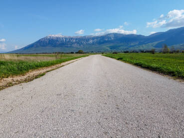 Duga ravna cesta u polju sa planinama u pozadini. Duga ravna cesta u polju sa planinama u pozadini. Livanjsko polje i planina Kamešnica.