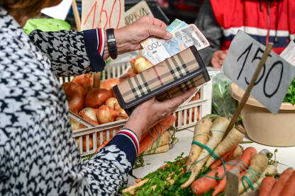 Žena plaća kupljeno voće i povrće na pijaci. Žena drži novac i novčanik u ruci. Osoba kupuje hranu i namirnice.
