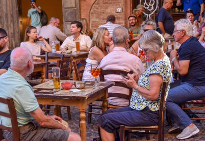 Ljudi uživaju u svom piću u bašti lokala u Italiji. Kafić u Italiji pun gostiju. Turisti piju piće.