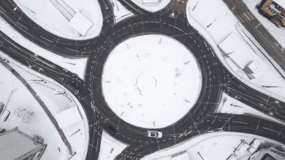 Automobili i kamioni se kreću u kružnom toku zimi. Snimak dronom na kružni tok u gradu tokom snježnih padavina.