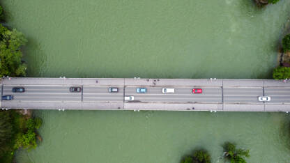 Most iznad mutne rijeke. Automobili i pješaci koji se kreću mostom, snimak dronom. Prijevoz. Betonski most preko vode.