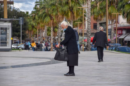 Starija žena stoji na ulici sa maskom na licu.