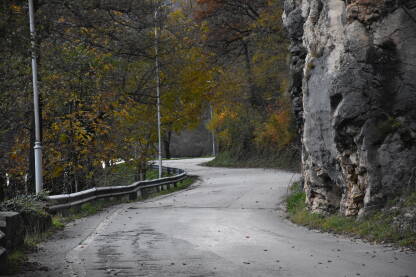 Asfaltirana cesta koja ide kroz prirodu sa stijenama sa desne strane i zelenilom i uličnom rasvjetom sa lijeve.