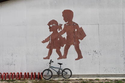 Mural na zidu škole, silueta dječaka i djevojčice, bicikl naslonjen na zid