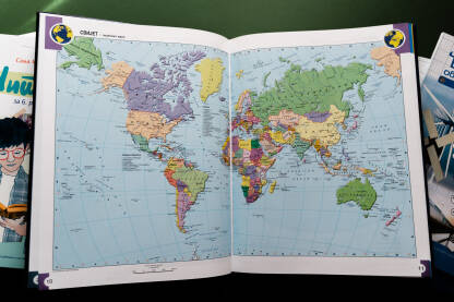 Atlas sa kartom svijeta, karta prikazuje različite zemlje i njihove lokacije. Knjiga je postavljena na zelenu površinu s pozadinom zelene boje.