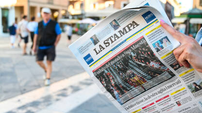 Djevojka drži novine na ulici. Osoba čita novine. Italijanska štampa. La Stampa.
