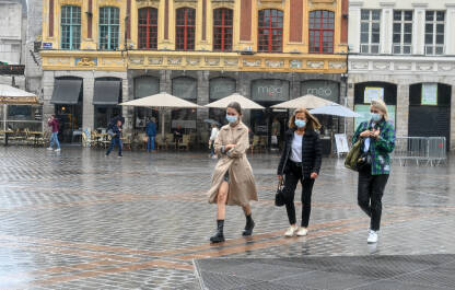 Žene sa maskama na licu šetaju ulicom tokom pandemije korona virusa. Djevojke hodaju po kiši. Žene sa maskama na licu šetaju ulicom. Pandemija korona virusa.