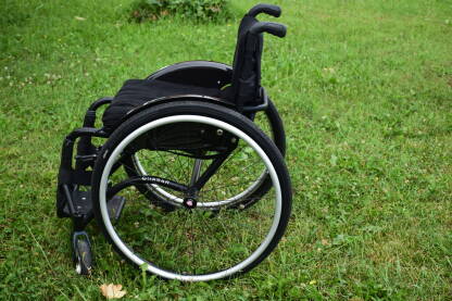 Crna invalidska kolica na livadi. Kolica su osnovno pomagalo ljudima koji imaju poteškoće sa kretanjem.