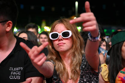 Djevojka se zabavlja na muzičkom festivalu. Mlada djevojka nosi naočale i pokazuje srednji prst na koncertu.
