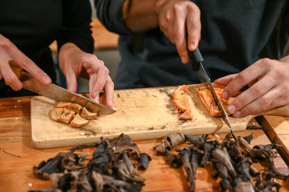Ljudi režu svježe divlje gljive za drvenim stolom. Priprema pečuraka za ručak. Rezanje gljiva.