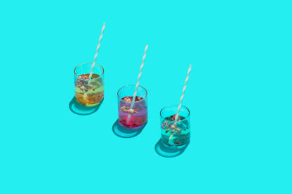 Tri čaše u bojama s pićem, začinima i papirnom slamkom na plavoj pozadini.