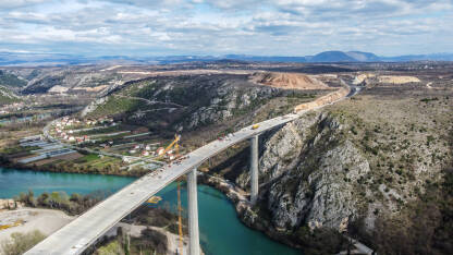 Izgradnja visokog mosta preko rijeke, snimak dronom. Radnici i mašine na gradilištu. Most na autoputu Vc kod Počitelja, BiH.