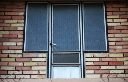 Metalna vrata sa prozorima sa strane, cigle raznih boja na zidu kuce