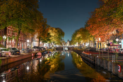 Amsterdam, Nizozemska. Zgrade, drveće, ulica i kanal u Amsterdamu noću. Grad navečer. Tipične i tradicionalne holandske  kuće.