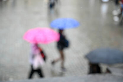 Zamagljeni ljudi sa kišobranom šetaju gradom po kiši. Kiša pada.