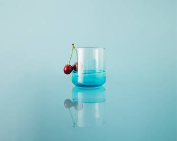 Čaša za piće sa svježim trešnjama na reflektirajućoj pozadini.
