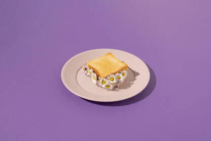 Tost sendvič s cvijećem tretinčice serviran na plastičnu tanjuru s ljubičastom pozadinom.
