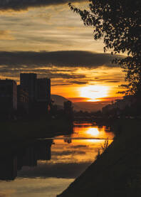 Fotografija nastala u Sarajevskom naselju Otoka. Trenutak zalaska sunca sa refleksijom na vodenu površinu rijeke Miljacke.