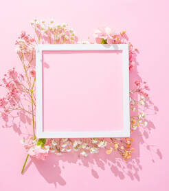Svijetli kreativni aranžman od svježih cvjetova karanfila i gipsofile na roze podlozi sa fotookvirom.