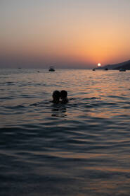 Odrasla osoba i dijete na kupanju u Jadranskom moru u sumrak, pred zalazak sunca