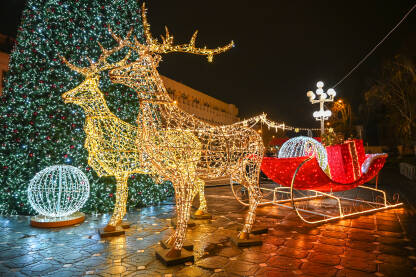 Osvijetljene saonice Djeda Mraza. Okićeno drvo u centru grada noću. Šareni ukrasi i svjetla na zimzelenom drvetu.