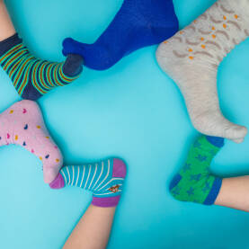 Stopala djece i roditelja sa raznobojnim čarapićima na svijetloj plavj podlozi sa praznim prostorom u sredini.