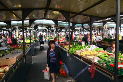 Ljudi kupuju svježe voće i povrće na pijaci. Žena sa torbom traži namirnice na pijaci.