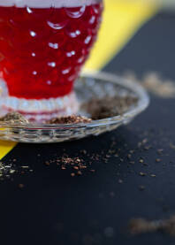 Staklena šoljica crvenog čaja na crno - žutoj postavi posutoj sa suhim travama čaja