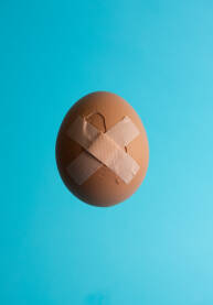 Razbijeno jaje izbliza, close up, sa flasterom na svijetloplavoj podlozi. Rana, ranjavanje, povreda, zaštita, obnavljanje, zarastanje - koncept.