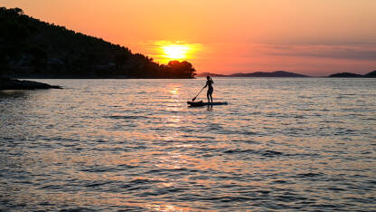 Djevojka vesla na dasci na moru. Žena uživa na Paddle-boardu ljeti. Veslanje na mirnom moru na zalasku sunca.