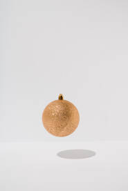 Sjajna, zlatna ukrasna kuglica koja lebdi iznad bijele pozadine. Božićna, novogodišnja čestitka.