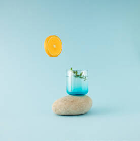 Staklena čaša za piće napunjena vodom i postavljena na kamen s kriškom naranče kao sunce.
