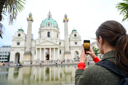 Beč, Austrija: Djevojka fotografiše crkvu svojim mobilnim telefonom. Turisti fotografišu ispred crkve i fontane u gradu. Crkva sv. Charlesa.