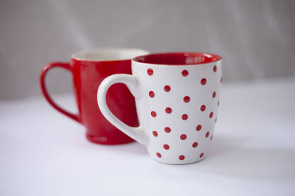 Dve soljice za kafu, jedna bele boje sa crvenim tackicama spolja i crvenom bojom unutra, druga sa crvenom spoljasnoscu i belom bojom unutra