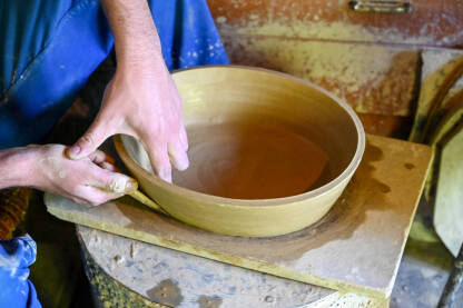 Majstor radi s glinom na grnčarskom kolu. Čovjek obrađuje glinu. Majstor pravi glinenu zdjelu. Obrada gline. Proizvodnja keramičkog posuđa od prirodnih materijala.