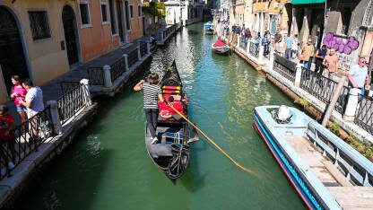 Venecija, Italija: Gondola na rijeci. Historijske građevine uz riječni kanal. Popularno turističko odredište. Turisti istražuju grad.