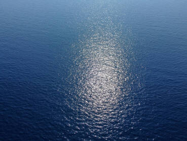 Površina plavog dubokog mora. Odraz sunca na površini vode. Snimak okeana iz aviona.