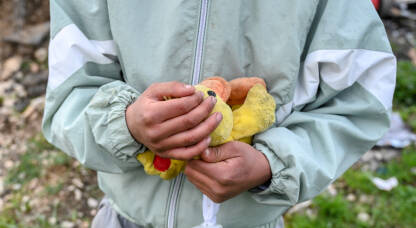 Siromašno dijete drži igračku. Dječak s plišanom žutom patkom. Dijete čvrsto drži plišanu igračku patku.