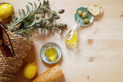 Maslinovo ulje na stolu sa maslinama, limunom, maslinovom granom i baguette-om