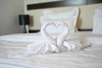 Labudovi napravljeni od bijelog peškira u hotelskoj sobi. Dekoracija na krevetu u motelu. Ručnik presavijen u obliku labuda.
