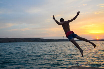 Mladić skače u more. Čovjek skače u vodu na zalasku sunca.