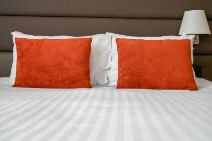 Krevet pripremljen za spavanje. Bijeli i crveni jastuci i bijeli jorgan na krevetu u hotelskoj sobi. Uredan krevet u apartmanu.