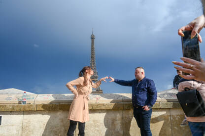 Pariz, Francuska: Zaljubljeni par u gradu ljubavi. Turisti se fotografišu sa Ajfelovim tornjem u pozadini.