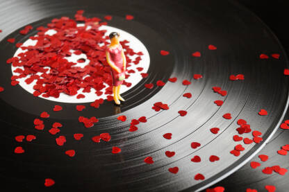 Figurica žene koja stoji na gramofonskoj ploci posutoj sitnim crvenim srcima.