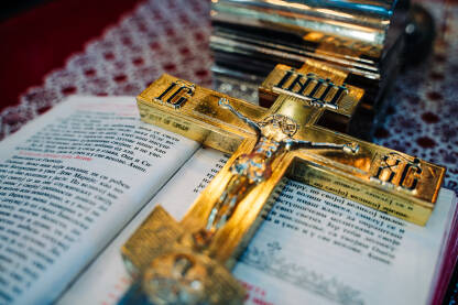 Zlatni pravoslavni krst na vrhu otvorene Biblije na stolu. Zlatni sjaj krsta dodaje dubinu i duhovnu dimenziju sceni.