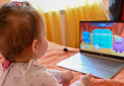 Djevojčica sjedi na krevetu i gleda crtani na laptopu. Beba gleda crtaće na računaru.