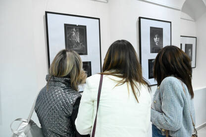 Posjetioci posmatraju fotografije u galeriji. Ljudi na izložbi. Posjetioci posmatraju i fotografišu fotografije u galeriji.