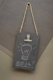Na slici je ručno napisan natpis "Ideja?" koji visi na crnoj tabli. Iznad natpisa je slika sijalice.