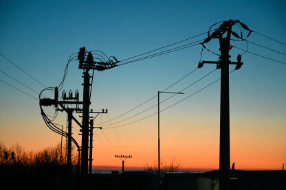 Električni stupovi sa žicama pri zalasku sunca. Prijenos električne energije. Stupovi i kablovi.